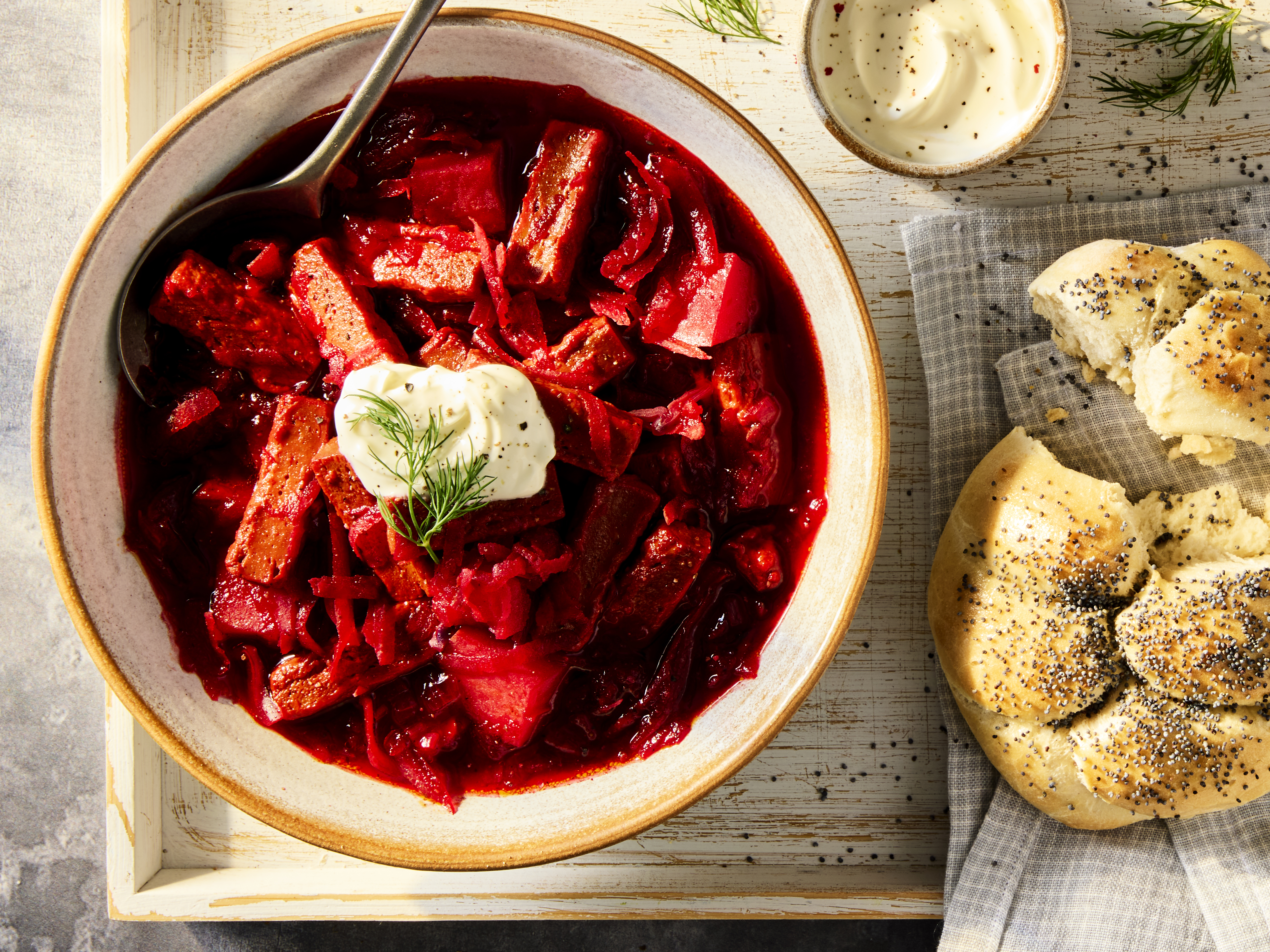 A vegetarian Borscht Soup with Quorn Steak Strips and beetroot, red cabbage and potatoes in a white bowl on a wooden background.
