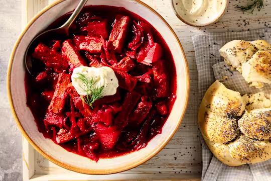 A vegetarian Borscht Soup with Quorn Steak Strips and beetroot, red cabbage and potatoes in a white bowl on a wooden background.