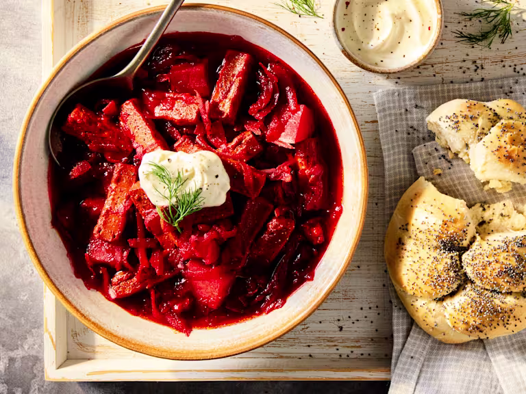 A vegetarian Borscht Soup with Quorn Steak Strips and beetroot, red cabbage and potatoes in a white bowl on a wooden background.
