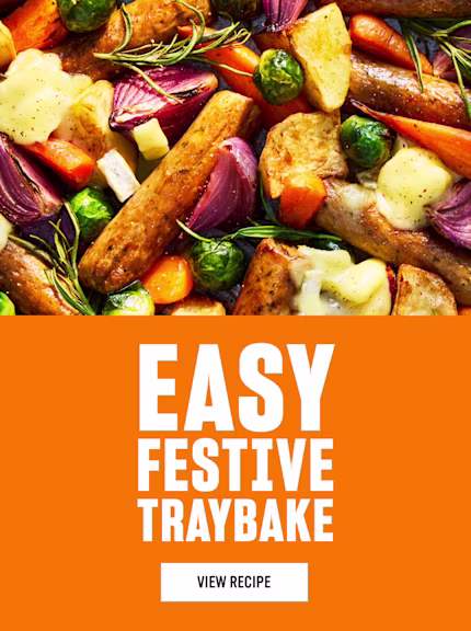 A colourful festive traybake of roasted sausages, potatoes, carrots, Brussels sprouts and red onions, topped with melted cheese and sprigs of rosemary, shown beside bright orange text reading “Easy Festive Traybake - View Recipe.