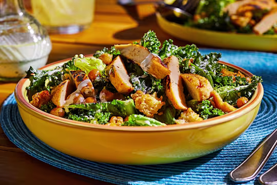 A bowl of vegan Caesar salad made with kale and cos lettuce topped with Quorn Meatless Fillets, chickpeas, and croutons.