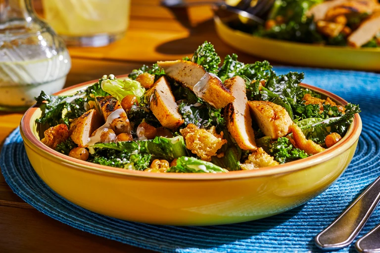 A bowl of vegan Caesar salad made with kale and cos lettuce topped with Quorn Meatless Fillets, chickpeas, and croutons.