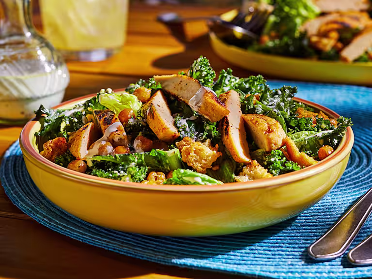 A bowl of vegan Caesar salad made with kale and cos lettuce topped with Quorn Meatless Fillets, chickpeas, and croutons.