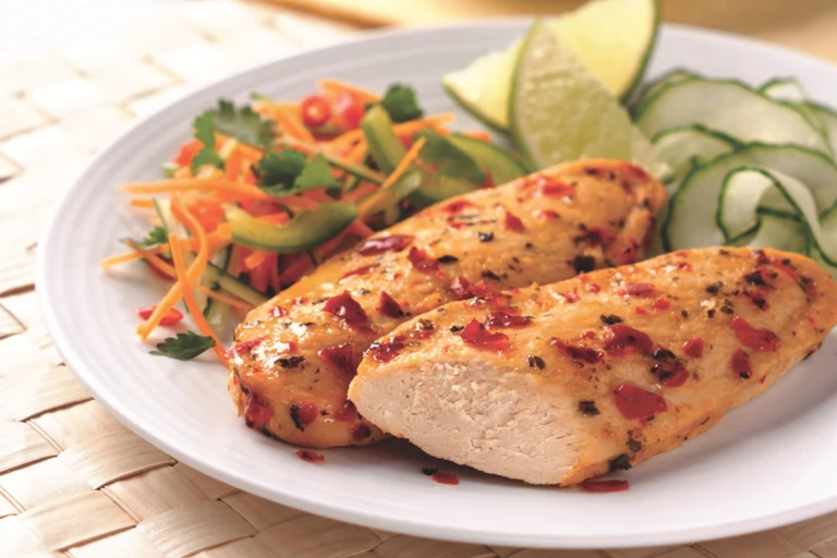 Two Quorn Fillets topped with a chili sauce with ribbons of zucchini, two wedges of lime, and a shredded carrot salad on the side.