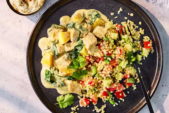 Creamy Spicy Mango Vegetarian Chicken with spinach, served on a dark plate alongside a fresh tomato and cucumber Tabbouleh salad.