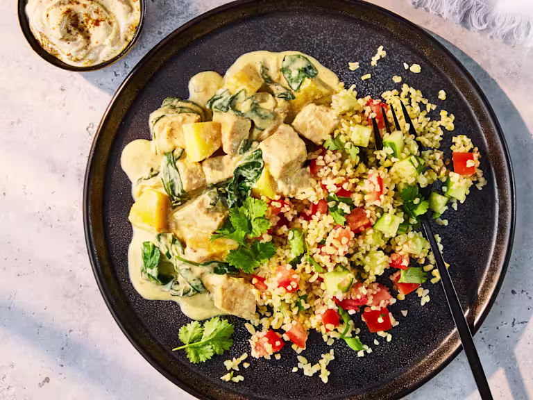Creamy Spicy Mango Vegetarian Chicken with spinach, served on a dark plate alongside a fresh tomato and cucumber Tabbouleh salad.