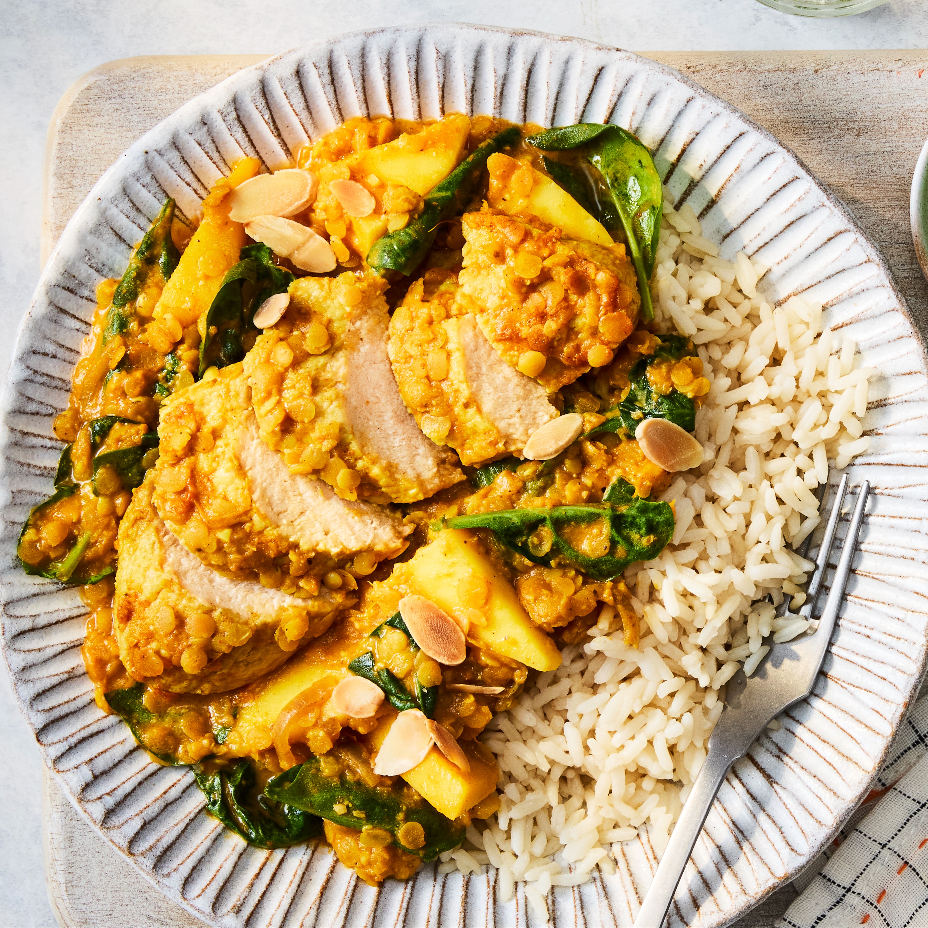 A Coconut & Lentil Vegetarian Chicken Curry with Quorn Fillets, almonds, onion, mango, spinach and rice on a white plate. 
