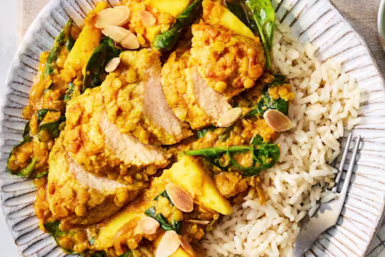 A Coconut & Lentil Vegetarian Chicken Curry with Quorn Fillets, almonds, onion, mango, spinach and rice on a white plate.