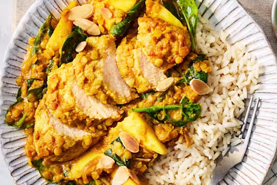 A Coconut & Lentil Vegetarian Chicken Curry with Quorn Fillets, almonds, onion, mango, spinach and rice on a white plate.