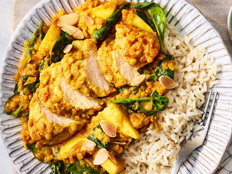 A Coconut & Lentil Vegetarian Chicken Curry with Quorn Fillets, almonds, onion, mango, spinach and rice on a white plate.