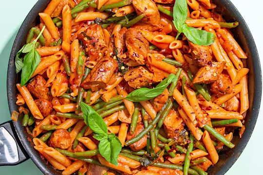 : Quorn Sausage Arrabiata pasta in a pan with basil leaves and green beans