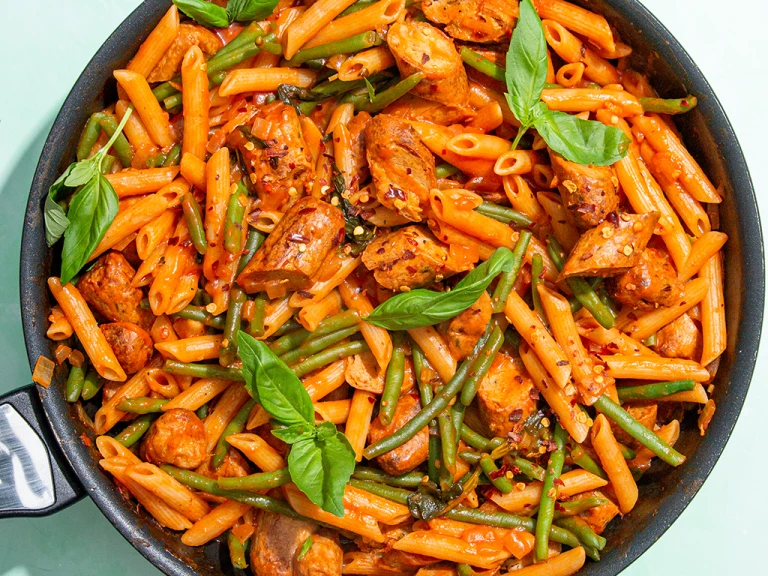 : Quorn Sausage Arrabiata pasta in a pan with basil leaves and green beans
