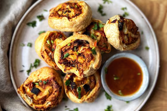 Masala pastry swirls on a plate served with coriander and hot dipping sauce in a bowl.