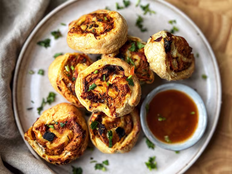Masala pastry swirls on a plate served with coriander and hot dipping sauce in a bowl.