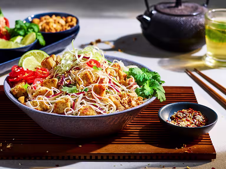 A white bowl of pad Thai noodles topped with green onions, chilis, Quorn Pieces and a sprig of cilantro.
