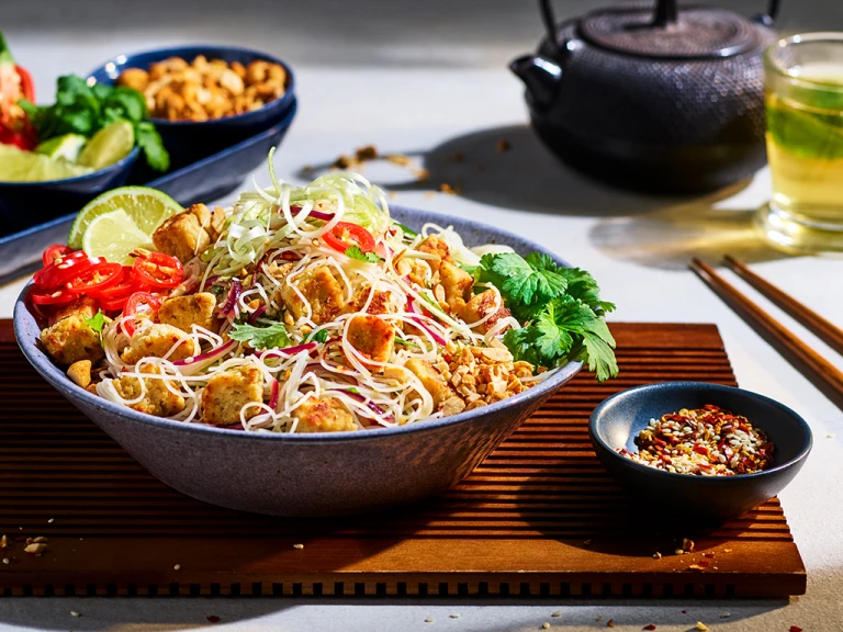 A white bowl of pad Thai noodles topped with green onions, chilis, Quorn Pieces and a sprig of cilantro. 