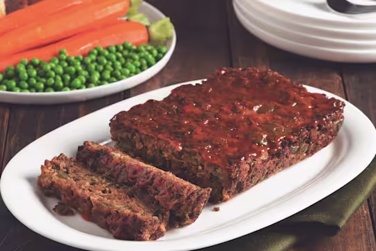 Quorn Vegetarian Meatloaf with two slices chopped served on a white dish with peas and carrots in the back.