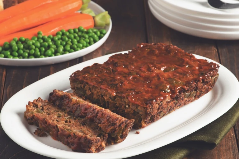 Quorn Vegetarian Meatloaf with two slices chopped served on a white dish with peas and carrots in the back.