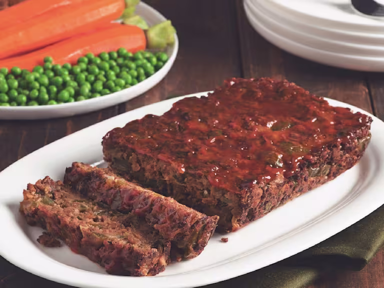Quorn Vegetarian Meatloaf with two slices chopped served on a white dish with peas and carrots in the back.