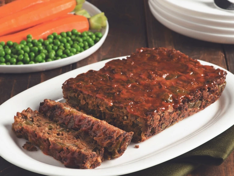 Quorn Vegetarian Meatloaf with two slices chopped served on a white dish with peas and carrots in the back.