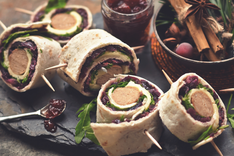 Five slices of a wrap filled with rocket, red cabbage slaw, cranberry sauce, brie, and Quorn Sausages.