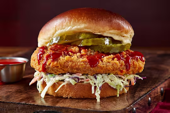 Vegetarian ChiQin Sandwich on a wooden slate with hot sauce