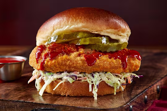 Vegetarian Chicken Sandwich on a wooden slate with hot sauce