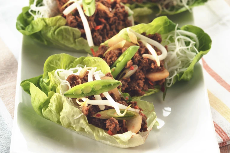 Three lettuce cups filled with Quorn Meatless Grounds, water chestnuts, and rice noodles, topped with bean sprouts and snow peas served on a white plate.