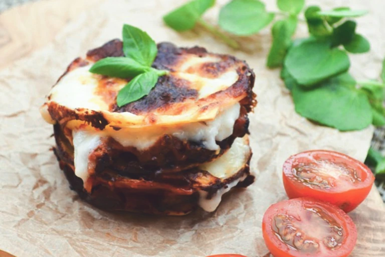 A circular, bite-sized stack of lasagna, Quorn Grounds, and cheese topped with basil and garnished with a halved cherry tomato.