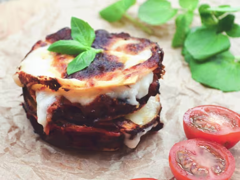 A circular, bite-sized stack of lasagna, Quorn Grounds, and cheese topped with basil and garnished with a halved cherry tomato.