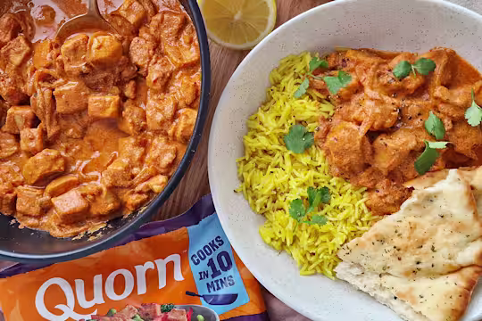 Butter chicken curry with yellow rice, naan bread and green garnish.