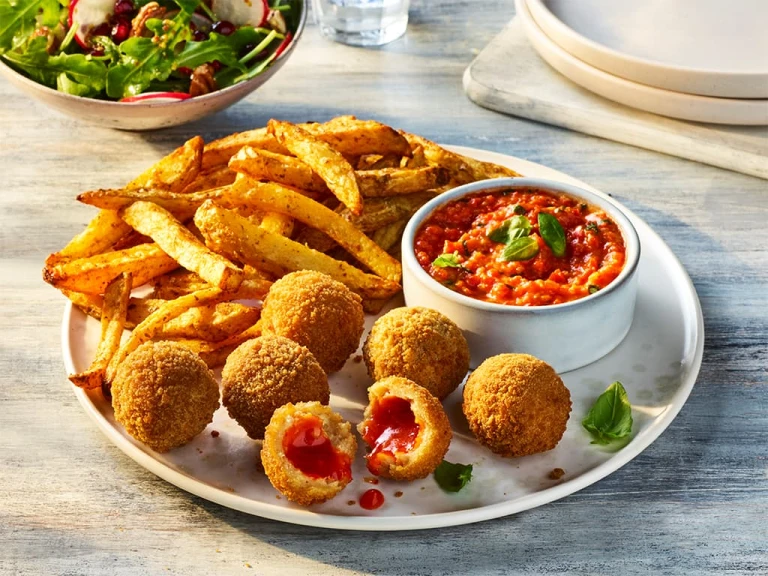 Air Fryer Veggie Chicken Balls with one split open to show the filling, served alongside roasted red pepper dip and fries.