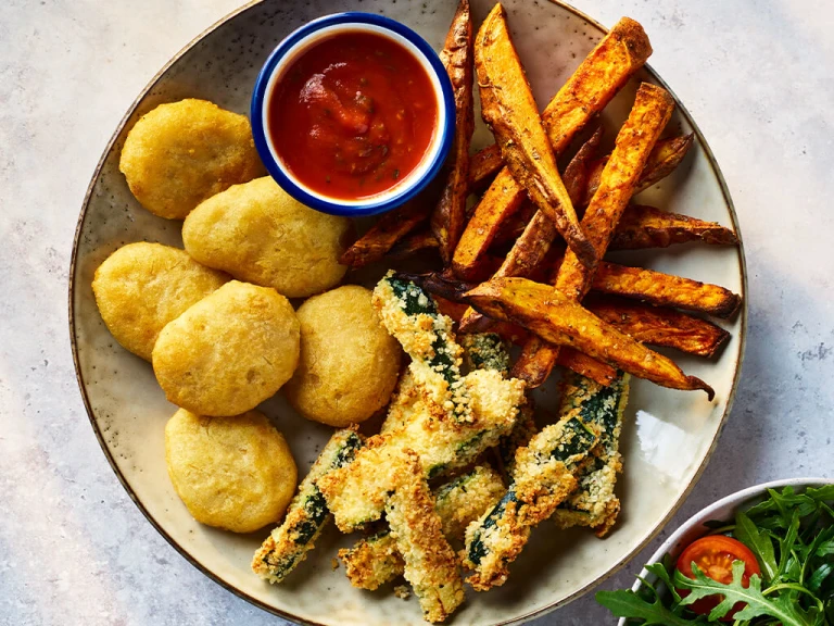 Quorn crispy nuggets with parmesan and garlic courgette chips on a board with sauce and salad on the side