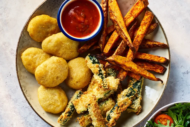 Quorn crispy nuggets with parmesan and garlic courgette chips on a board with sauce and salad on the side