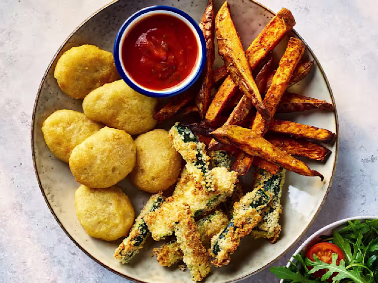 Quorn crispy nuggets with parmesan and garlic courgette chips on a board with sauce and salad on the side