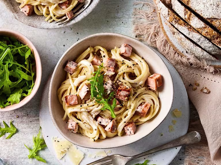A creamy vegetarian pasta carbonara made with Quorn pieces, garnished with fresh rocket and black pepper, served with crusty bread and a side of salad.