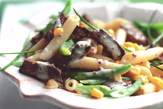 A serving of vegetarian creamy mustard pasta made with Quorn Vegetarian Steak Strips, fresh vegetables, and penne pasta in a white bowl.
