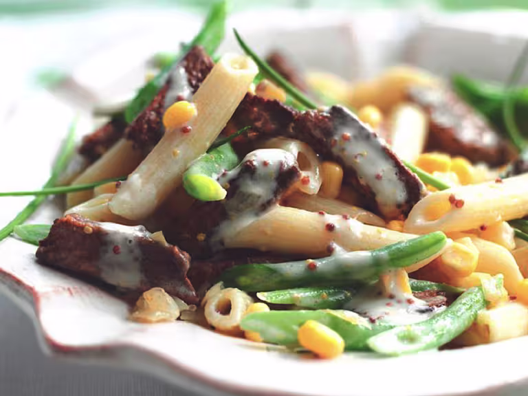 A serving of vegetarian creamy mustard pasta made with Quorn Vegetarian Steak Strips, fresh vegetables, and penne pasta in a white bowl.