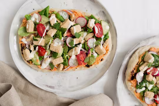 Flatbread topped with cucmbers, tomatoes, radishes, lettuce, hummus, mint, and Quorn Vegan Pieces.