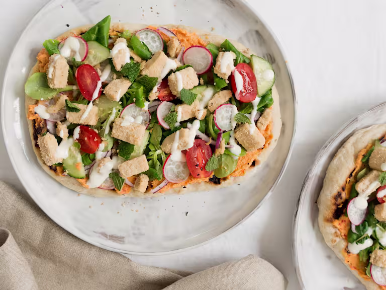 Flatbread topped with cucmbers, tomatoes, radishes, lettuce, hummus, mint, and Quorn Vegan Pieces.