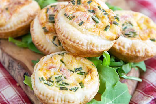 Mini veggie quiches made with Quorn Vegan Ham Slices served on a plate next to tomato slices topped with basil leaves and rocket.