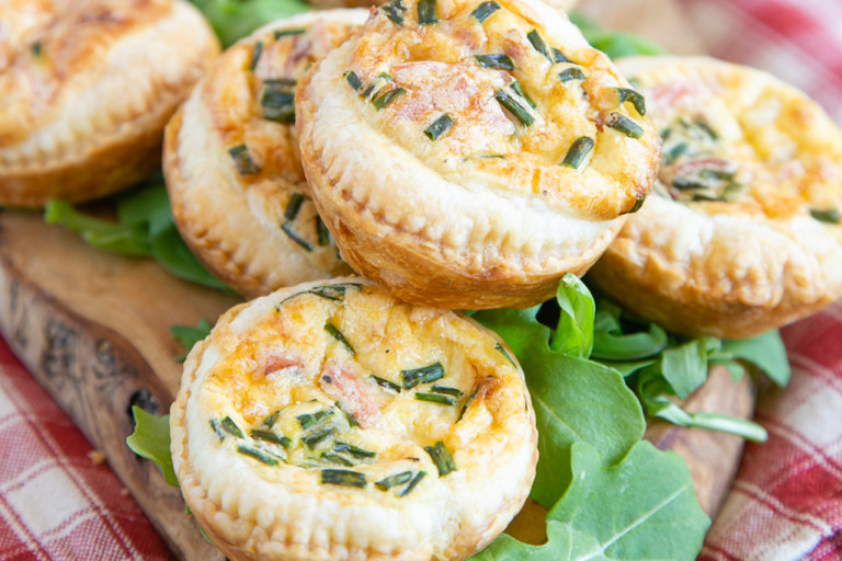 Mini veggie quiches made with Quorn Vegetarian Bacon served on a plate next to tomato slices topped with basil leaves and rocket