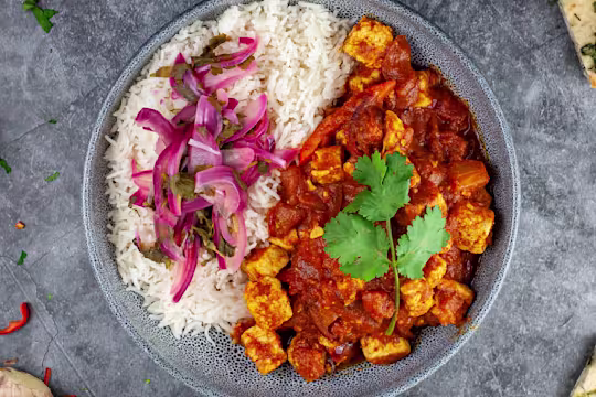 East Quorn curry with quick pickled red onion served in a bowl in naan and mango chutney on the side.