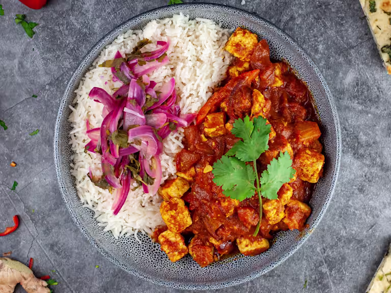 East Quorn curry with quick pickled red onion served in a bowl in naan and mango chutney on the side.