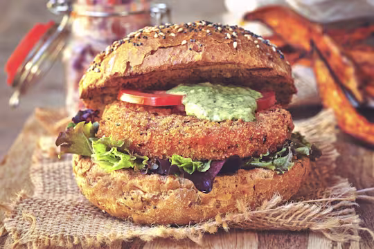 A Quorn Vegan Hot & Spicy Burger with pink slaw sat on a table beside sweet potato wedges.