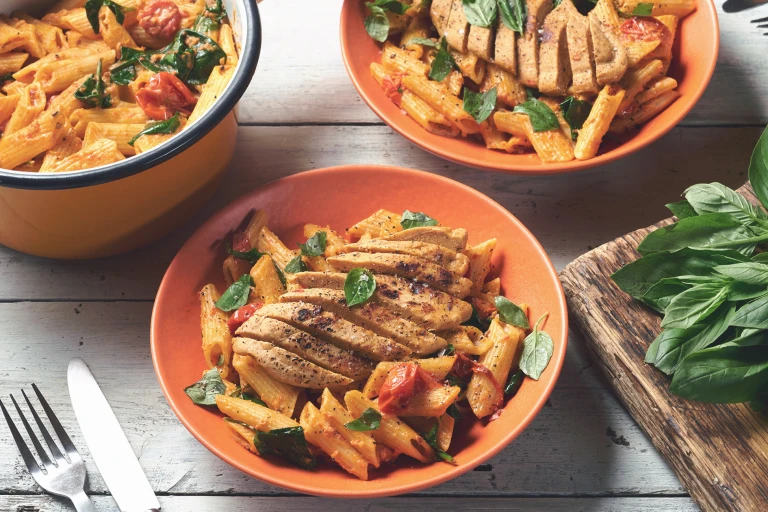 Bowls of pasta topped with Quorn Vegetarian Fillets and a pot of pasta on the side.