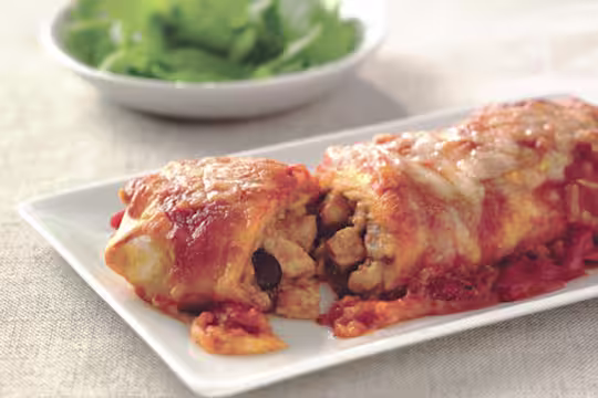 Vegetarian enchiladas made with Quorn Pieces, beans and cheese, sliced to reveal the centre, served on a white plate
