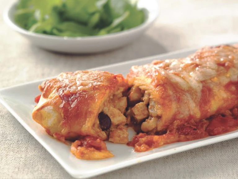 Vegetarian enchiladas made with Quorn Pieces, beans and cheese, sliced to reveal the centre, served on a white plate