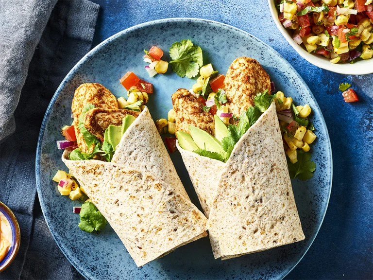 Quorn Jerk Style Mini Fillets and corn salsa in a wrap served on a blue dish with corn salsa on the side.