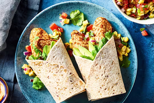 Quorn Tikka Style Mini Fillets and corn salsa in a wrap served on a blue dish with corn salsa on the side.